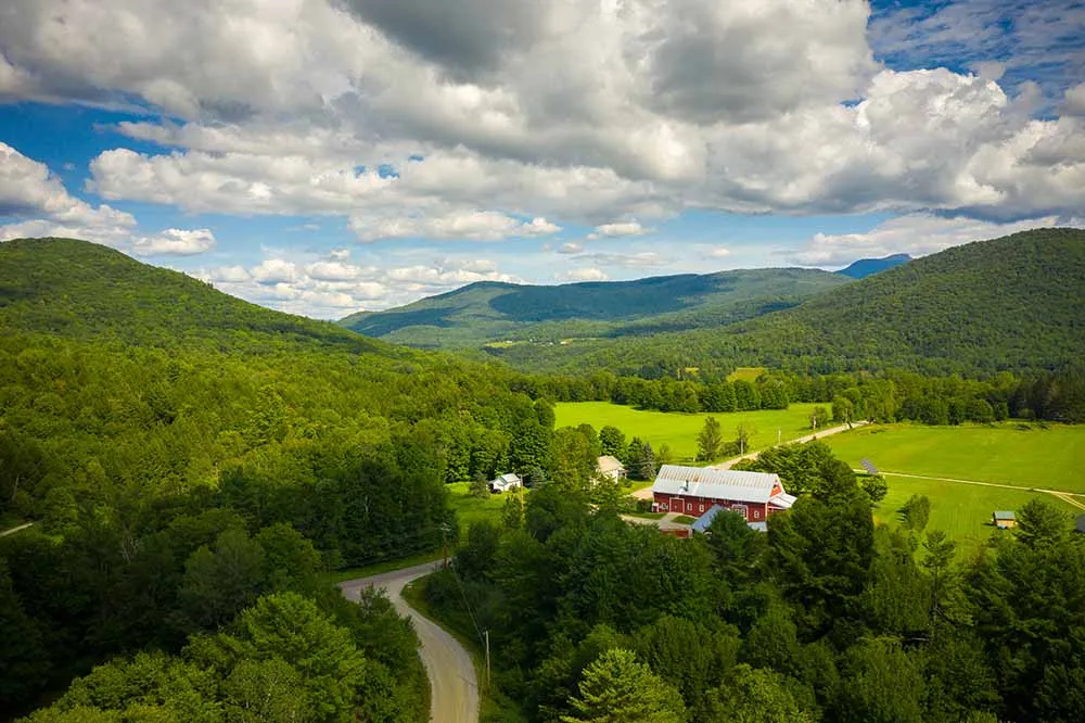 Aerial view of a red barn in Vermont surrounded by green fields on a sunny day.